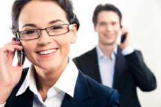 In the photo there is a man and a woman both on the telephone, looking happy and engaged in their job interview.